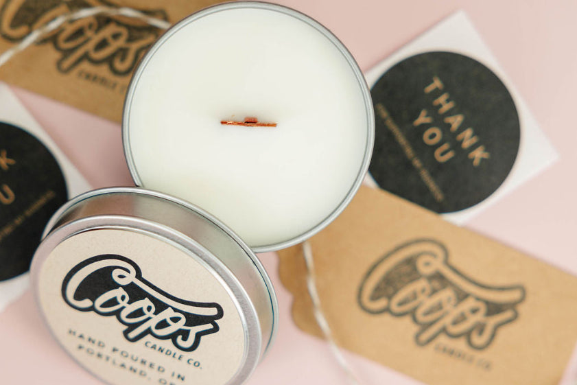 Coops candle with lid off on a pink background with branded materials.